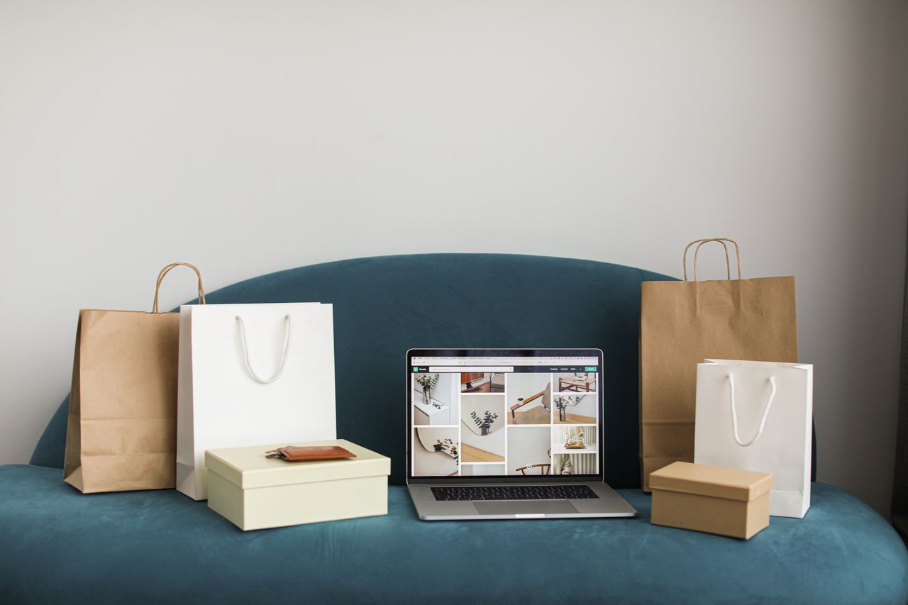 services-01 A laptop surrounded by shopping bags and boxes on a blue sofa, ideal for online shopping themes.