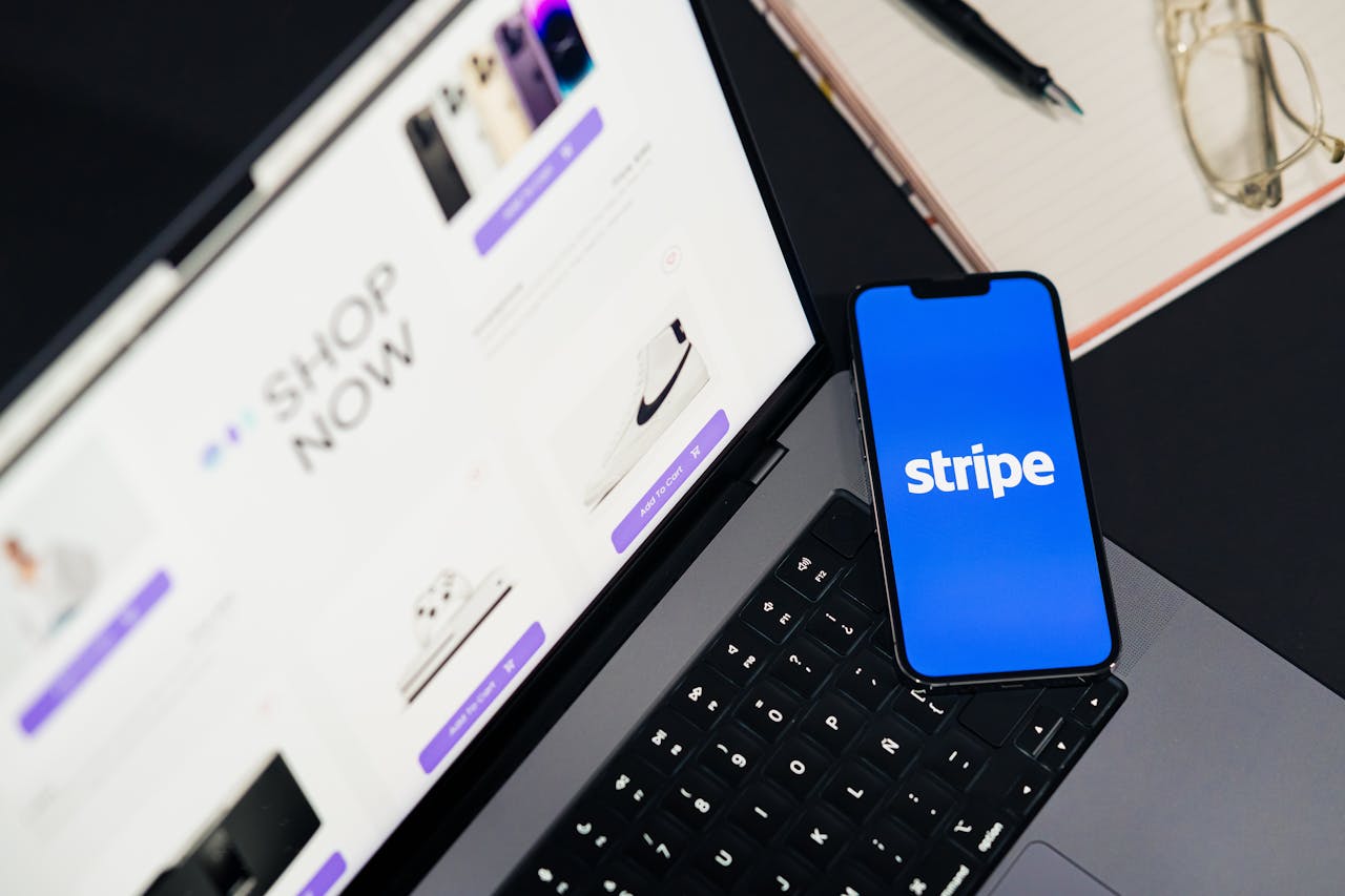 hero-img-02 Mobile phone displaying Stripe app on a laptop with an eCommerce site open, symbolizing online shopping.
